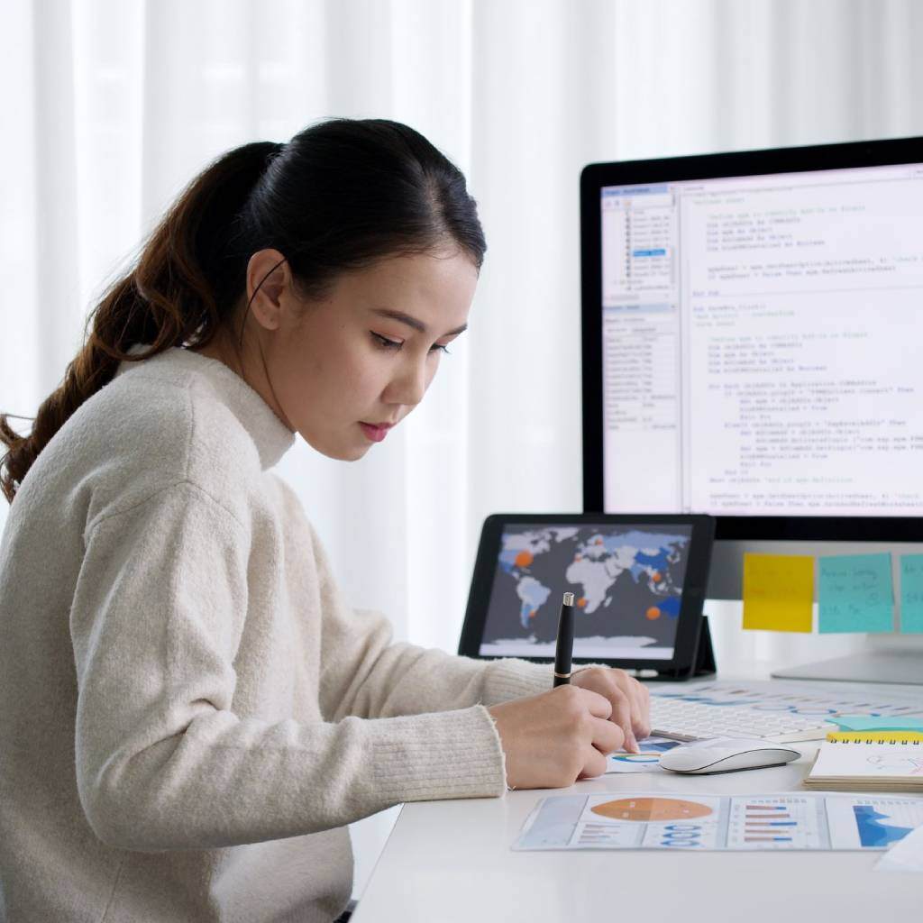 Data analyst reviewing reports and coding on a computer.