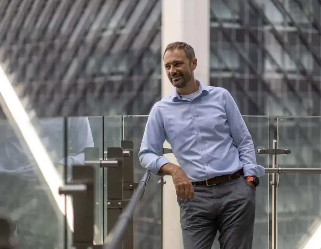 Business professional standing on a glass balcony in a modern urban setting.