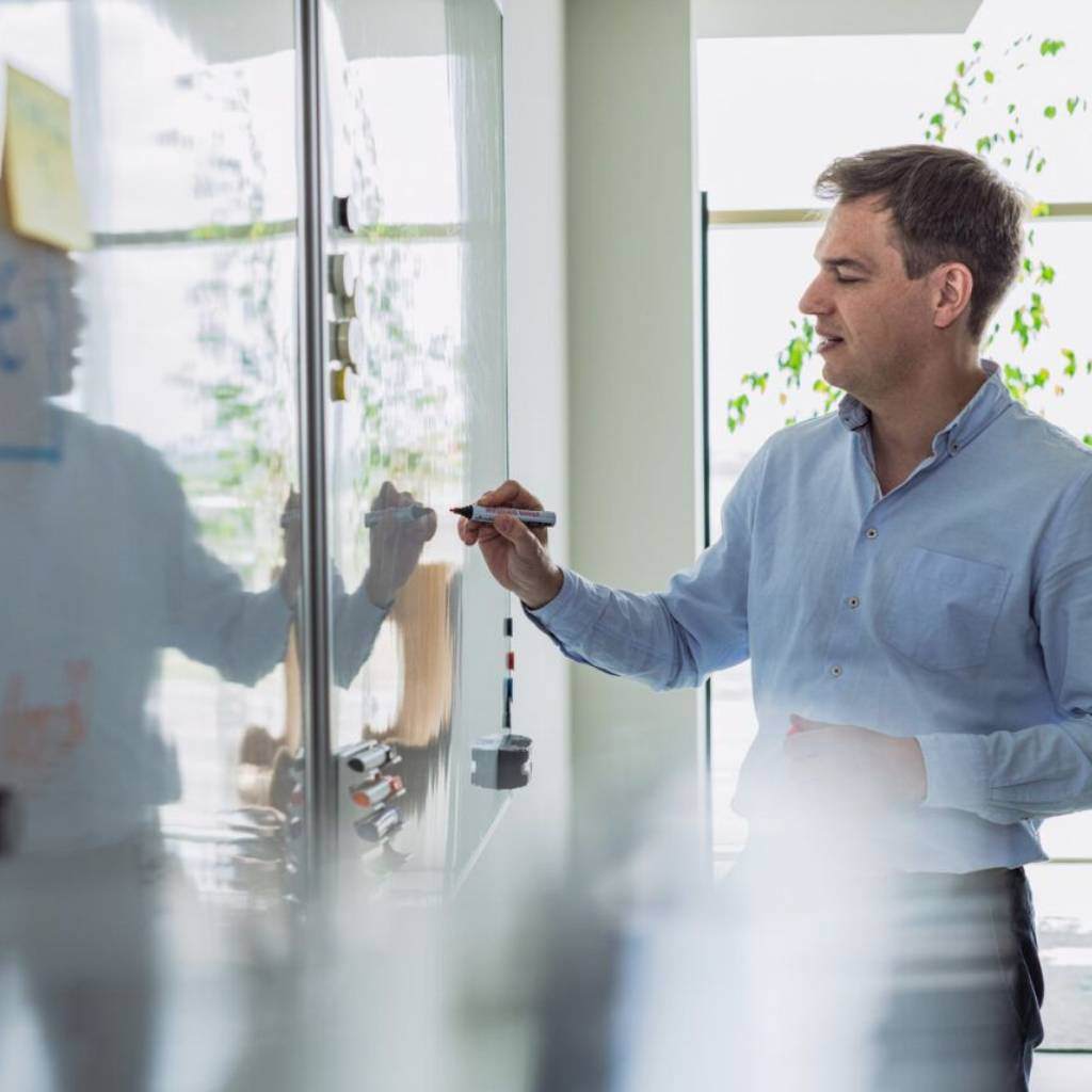 Data strategist brainstorming and writing on a whiteboard in a modern office.