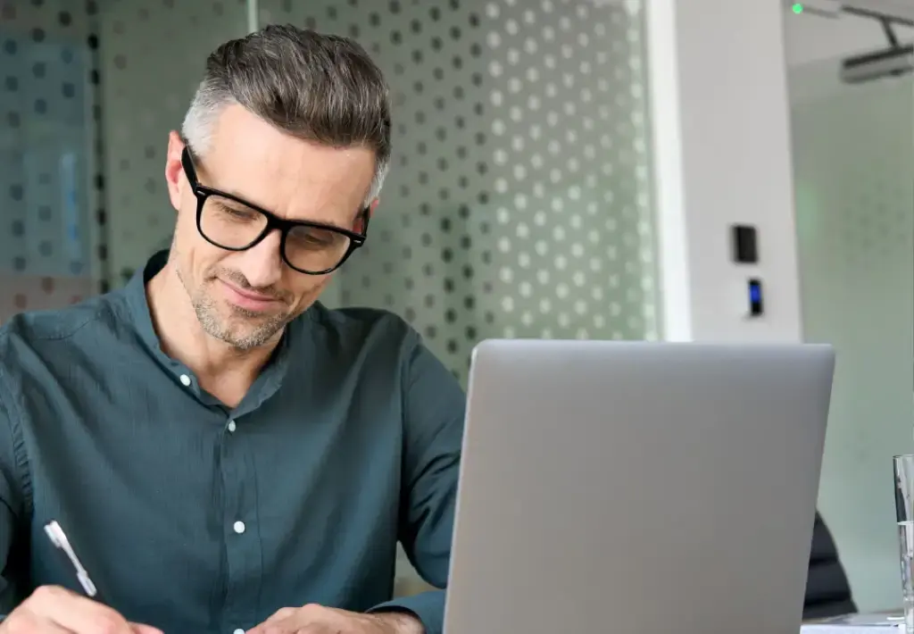  Professional taking notes while working on a laptop in a modern office.