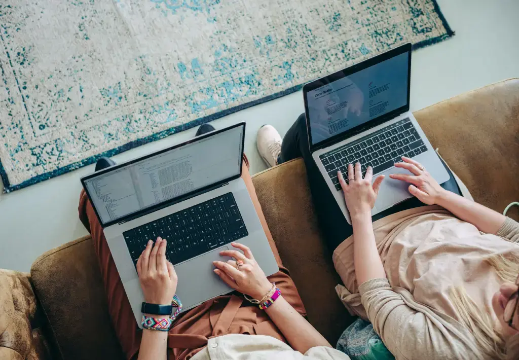 Two professionals working on laptops while seated on a couch.