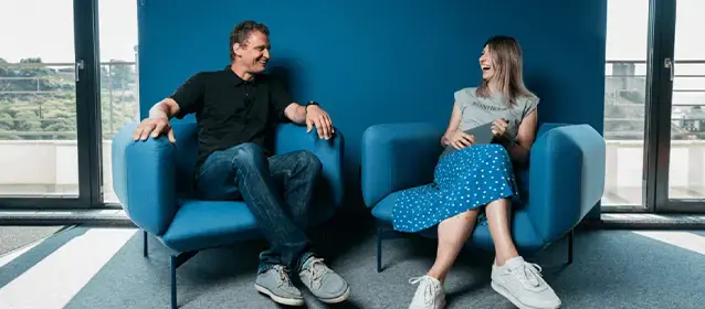 two endava employee engaged in lively discussion while sitting in blue chairs in blue office space