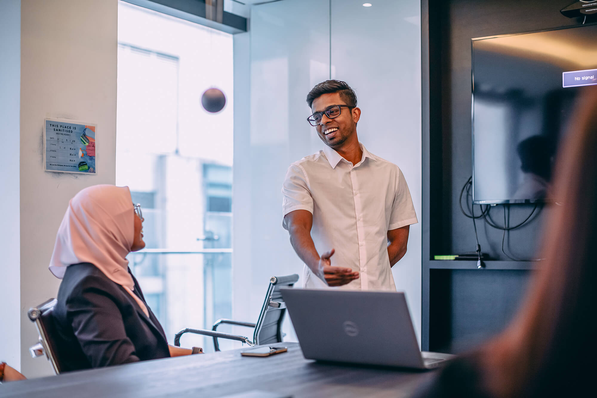 A professional presenting during a meeting in a modern office, engaging with seated colleagues around a table