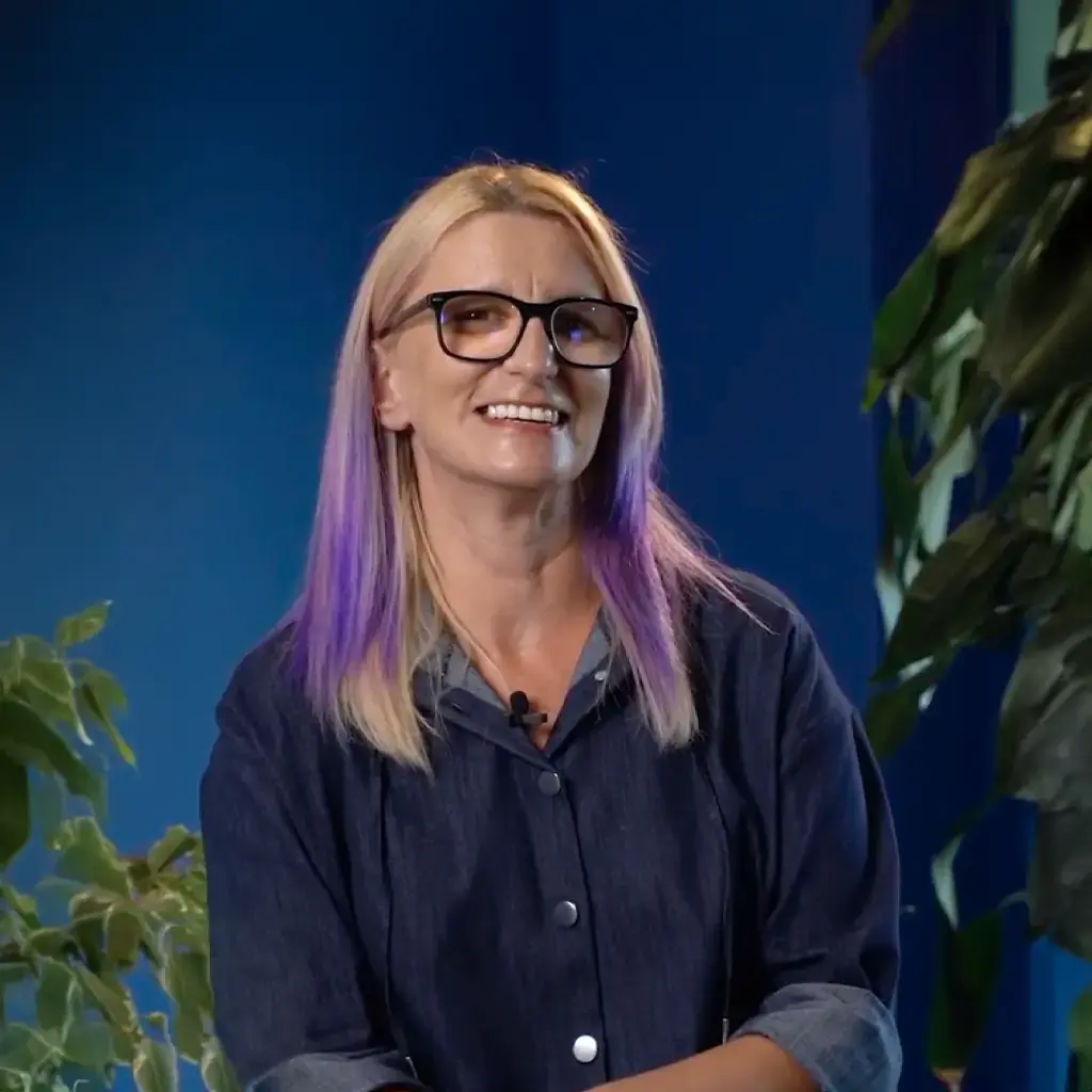 Business analyst smiling during an interview, with a blue background and greenery in the frame