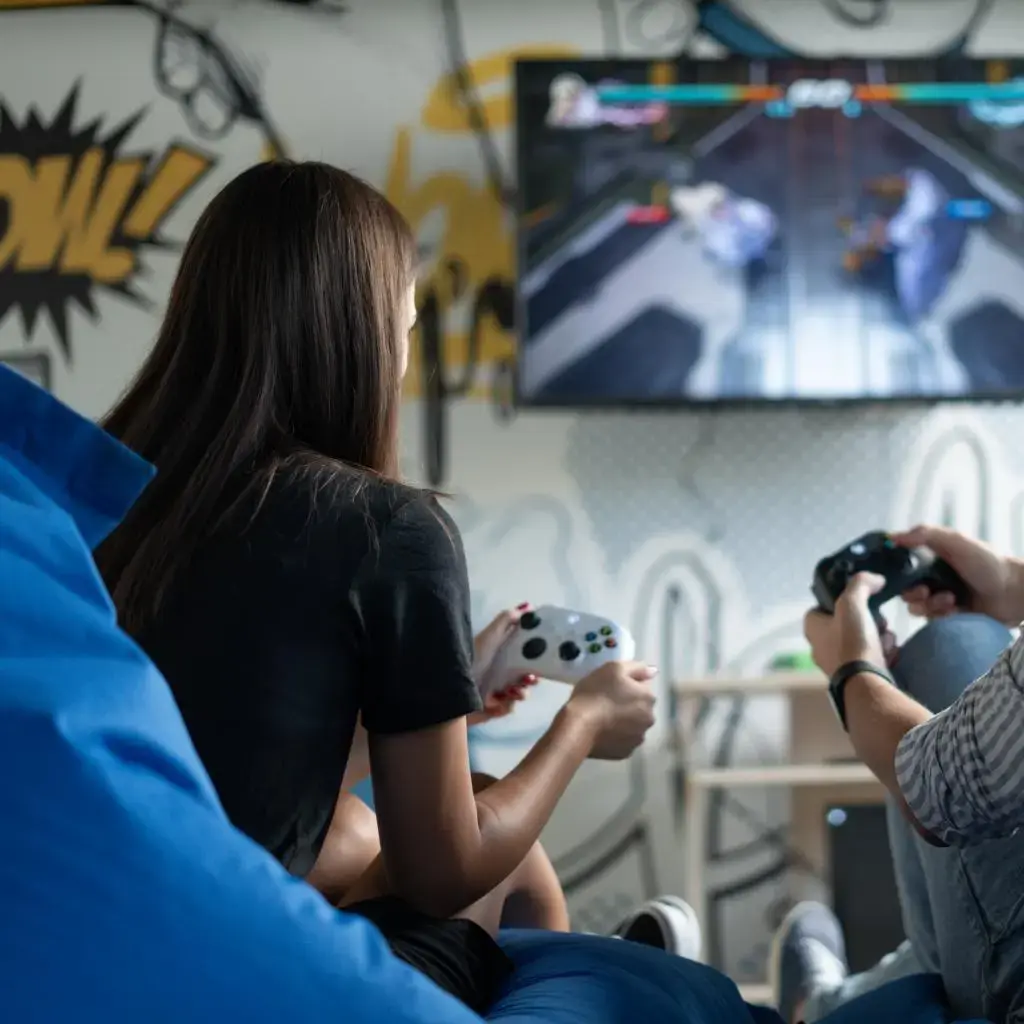 Two people sitting on beanbags playing a video game on a large screen in a modern office lounge.