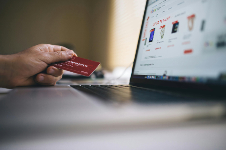 A hand with a card in front of a laptop