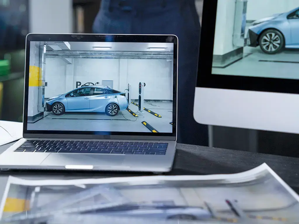 Professional analyzing an electric vehicle charging station simulation on laptop and desktop screens in an office.