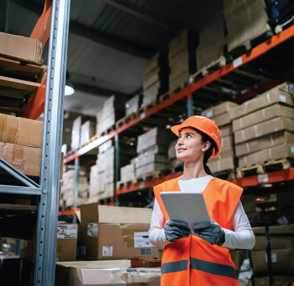 Warehouse worker in safety gear using a tablet to oversee inventory in a storage facility, highlighting management solutions