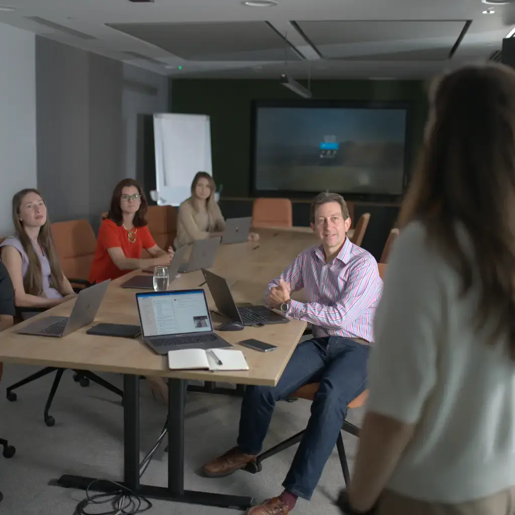 Team members in a modern conference room attentively listening to a presenter during a business meeting.