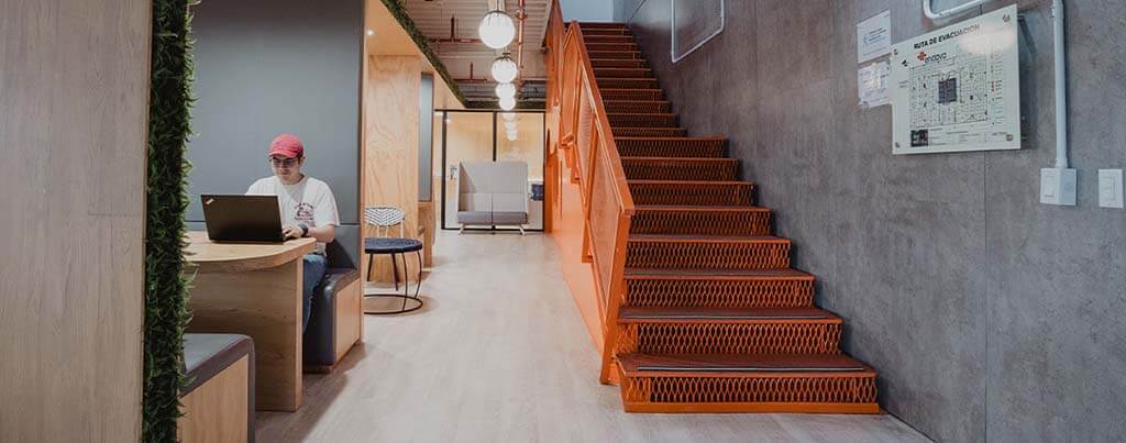 employee working on laptop at booth next to orange stairway leading upstairsup