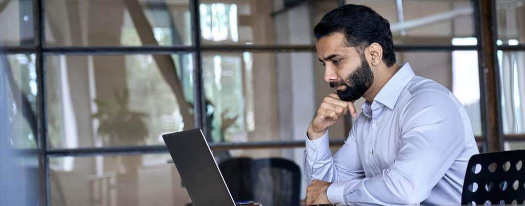 bearded male cyber security specialist looking at laptop