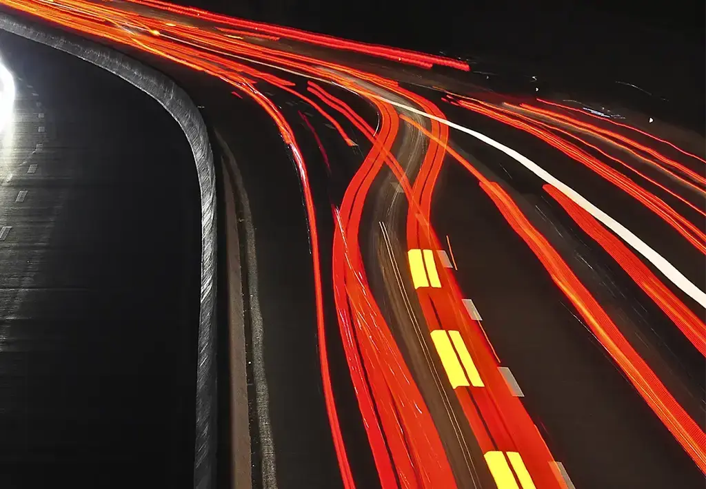 Long-exposure photo of a highway at night, showing white and red light trails from moving vehicles.