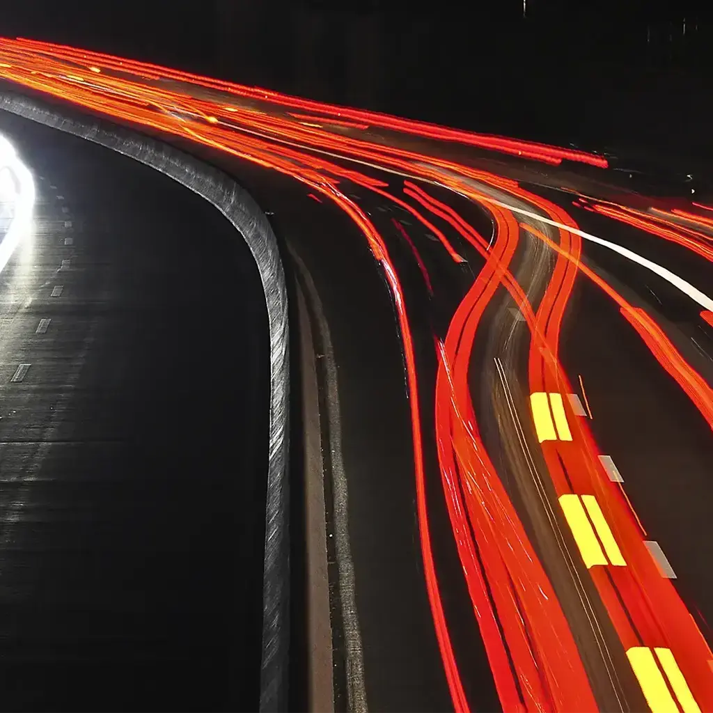 Long-exposure photo of a highway at night, showing white and red light trails from moving vehicles.