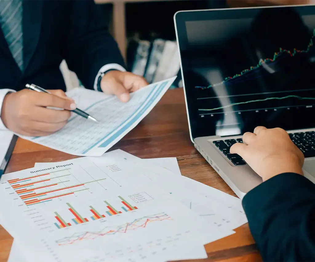 two banking business people reviewing charts on paper and on a laptop