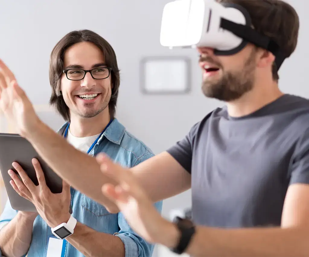 man testing a vr headset while his friend watches and holds a tablet