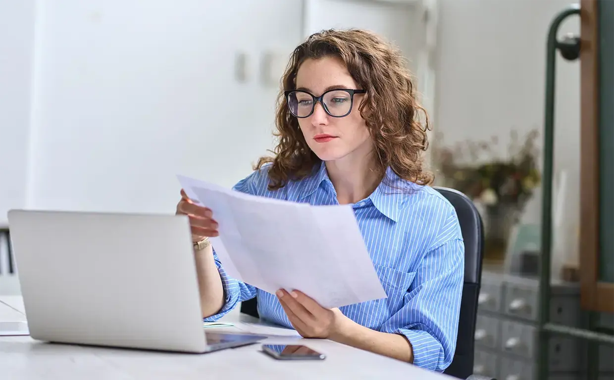 woman sitting at tablet in her home reviewing insurance paperwork in front of laptop