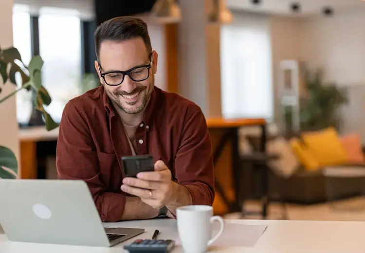 man reviewing payments on his phone while paying bills on laptop