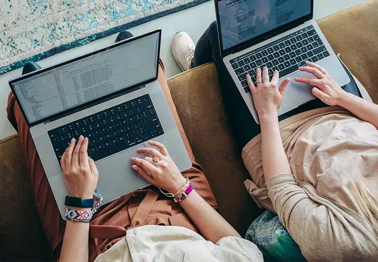 two women working together on laptops while sitting on a couch