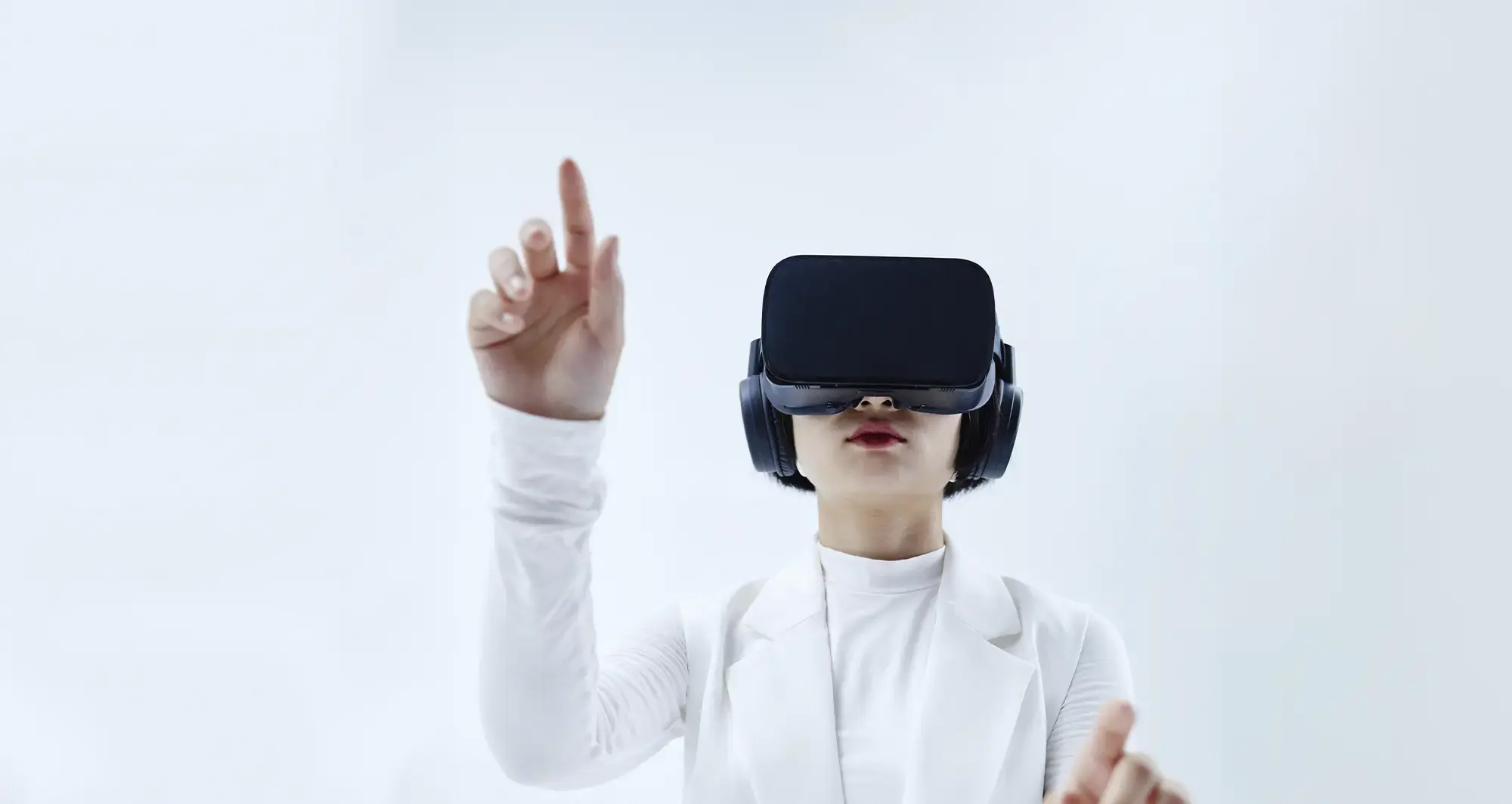 woman wearing all white and a vr headset is pointing up with her hand in the air