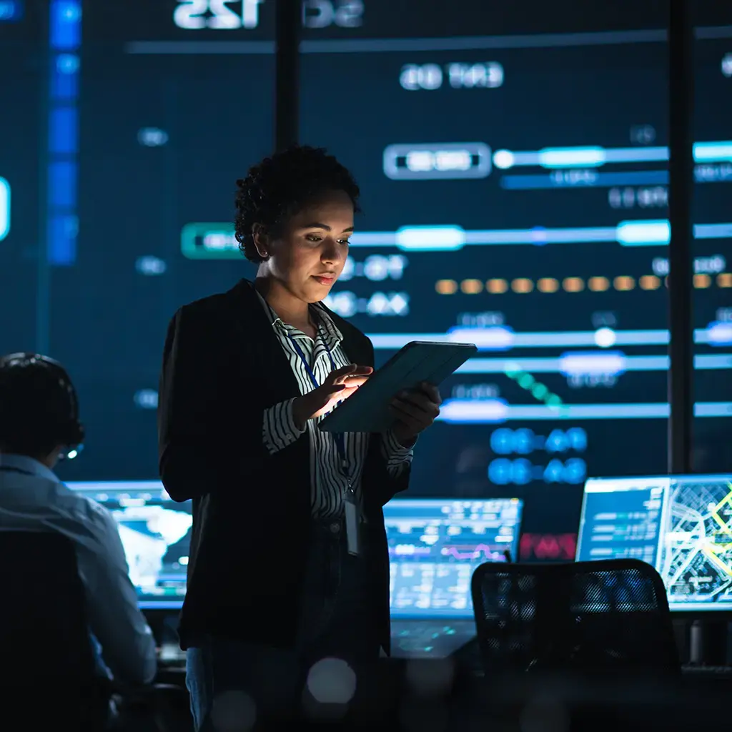 woman woking on tablet in front of computer screens in operations room