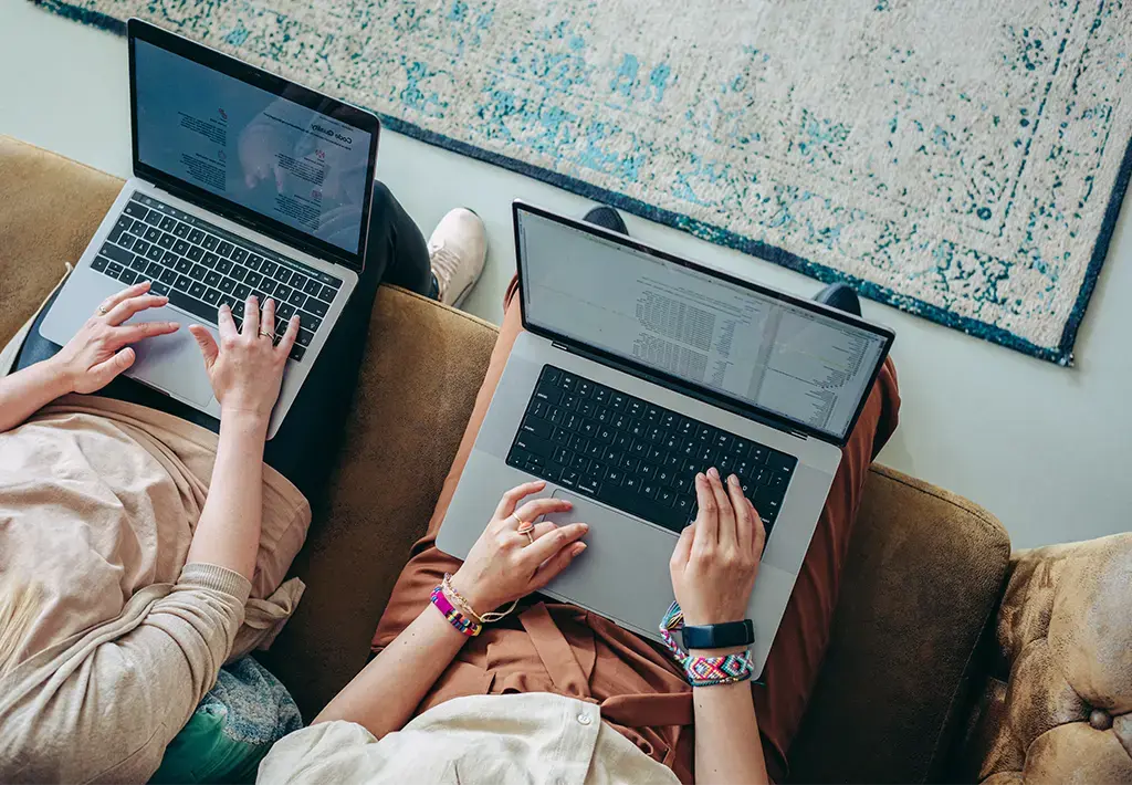 two women working on laptops while sitting on office couch