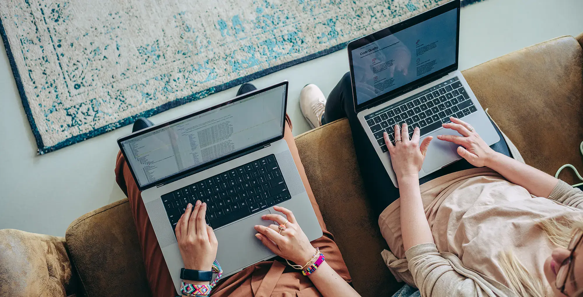 downward view of two women working on laptops on a brown couch