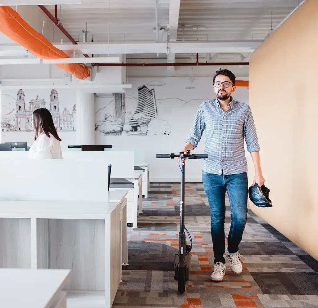 Man leaving the office while walking his scooter and helmet in hand