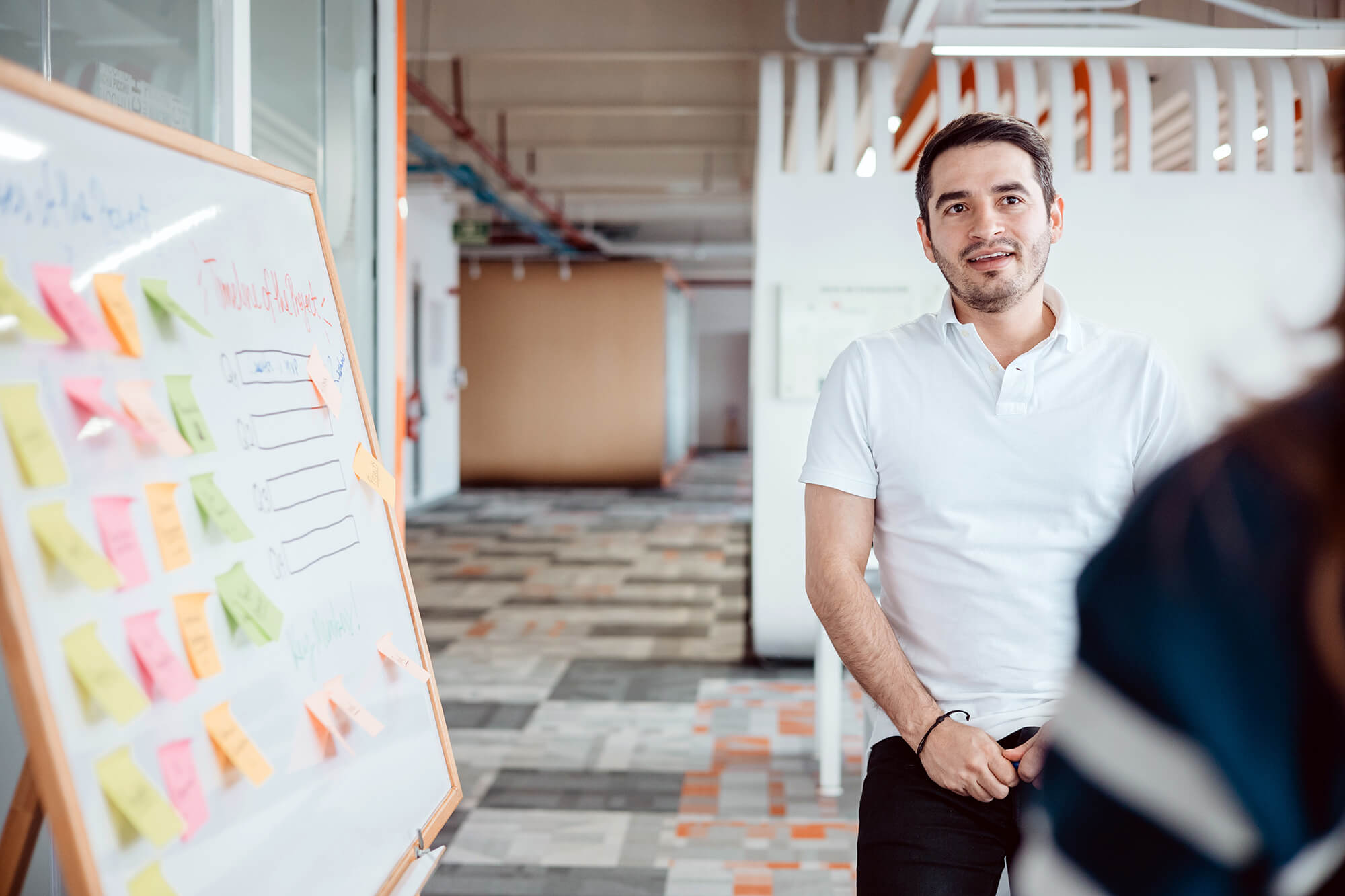 A professional presenting ideas using a whiteboard with sticky notes in a bright, open office space.