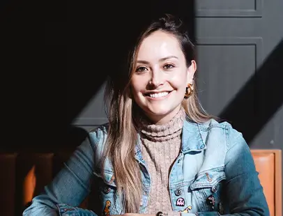 A professional seated at a wooden table, smiling in natural light with a dark background.