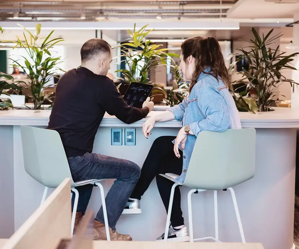 man holds tablet at desk with female coworker