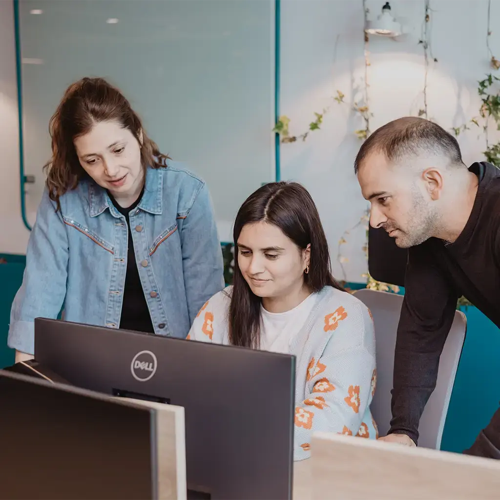 Three colleagues collaborating at a workstation in a modern office, discussing a project on a computer screen.