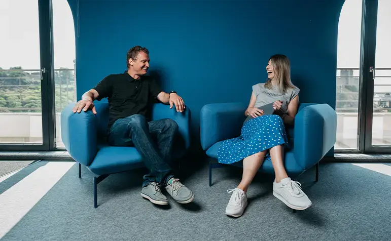 man and woman sitting in blue chairs in blue office laughing