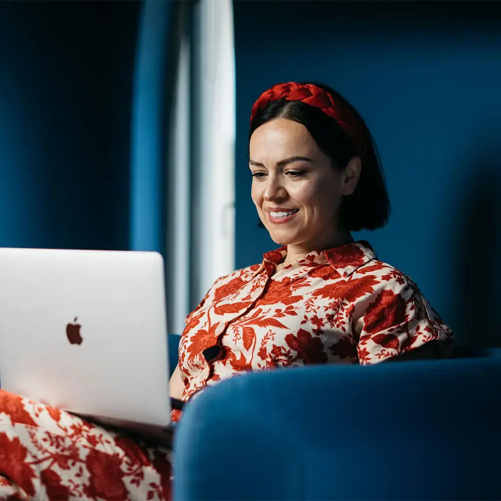 endava female employee sitting in blue chair in blue office working on apple laptop