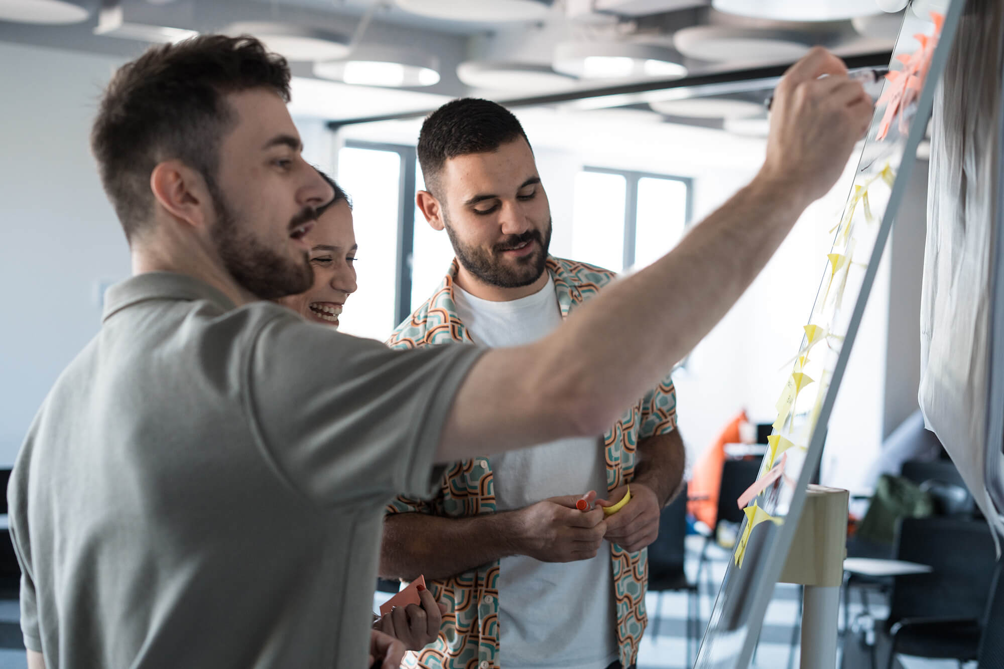 Team collaborating on ideas at a whiteboard in a modern office environment, using sticky notes for brainstorming