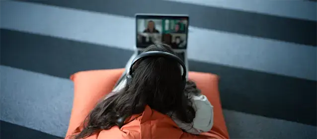 A person wearing headphones participating in a virtual meeting on a laptop while seated on a cushion.