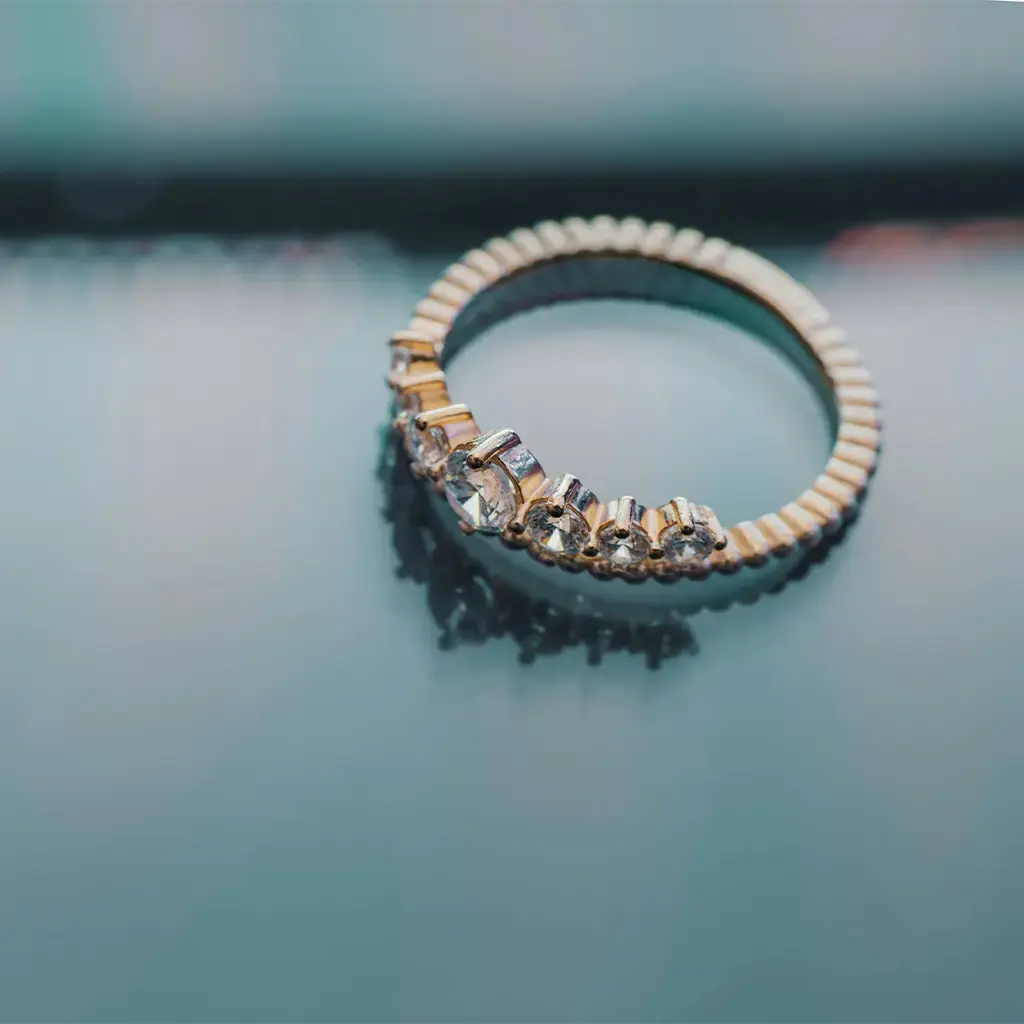 Gold ring with diamond accents displayed on a reflective surface, symbolizing luxury and retail craftsmanship.