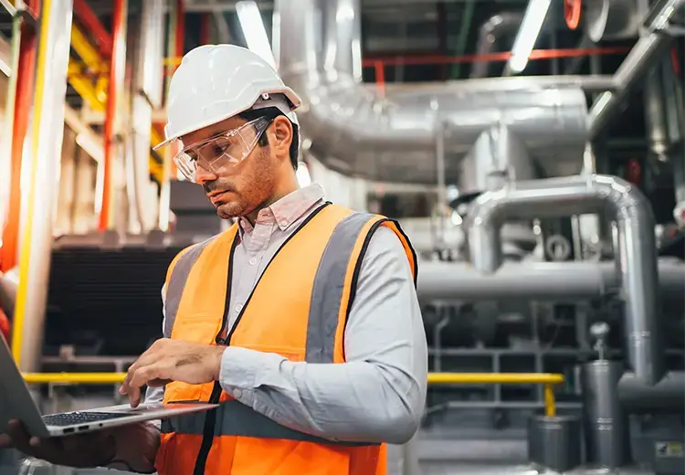 factory worker in orange vest checking data on laptop