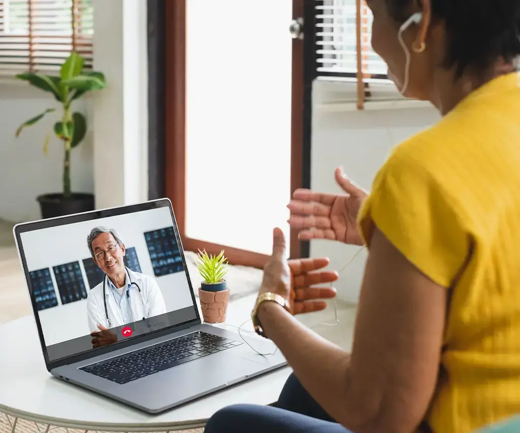 woman in yellow having healthcare virtual care visit from her home laptop