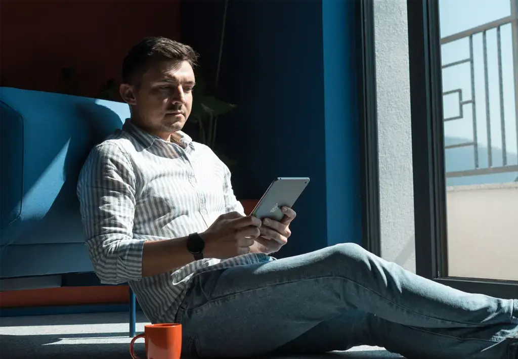 person viewing a tablet while relaxing on the floor by a sunny window