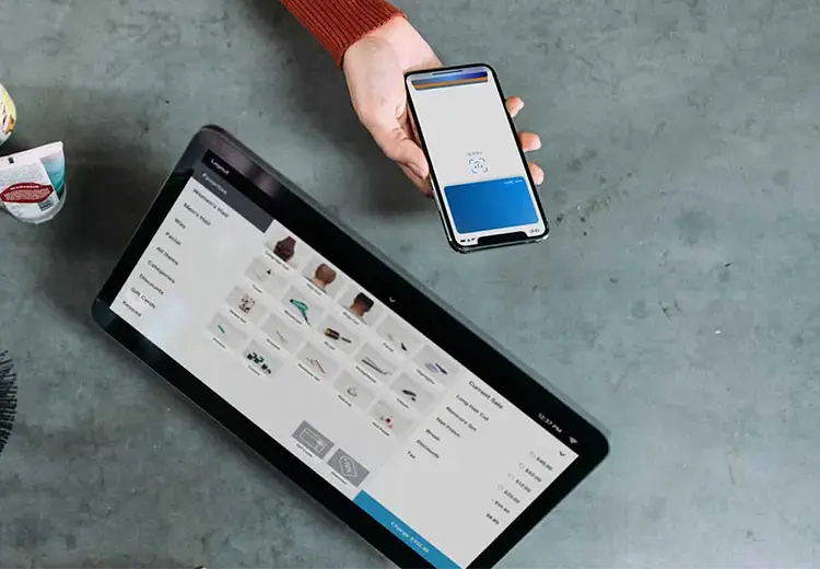 woman holding phone near retail payments tablet showing merchandise