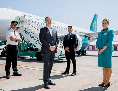 A diverse group of individuals posing in front of an airplane. Symbolizes Aer Lingus' modernized payment system for passengers.