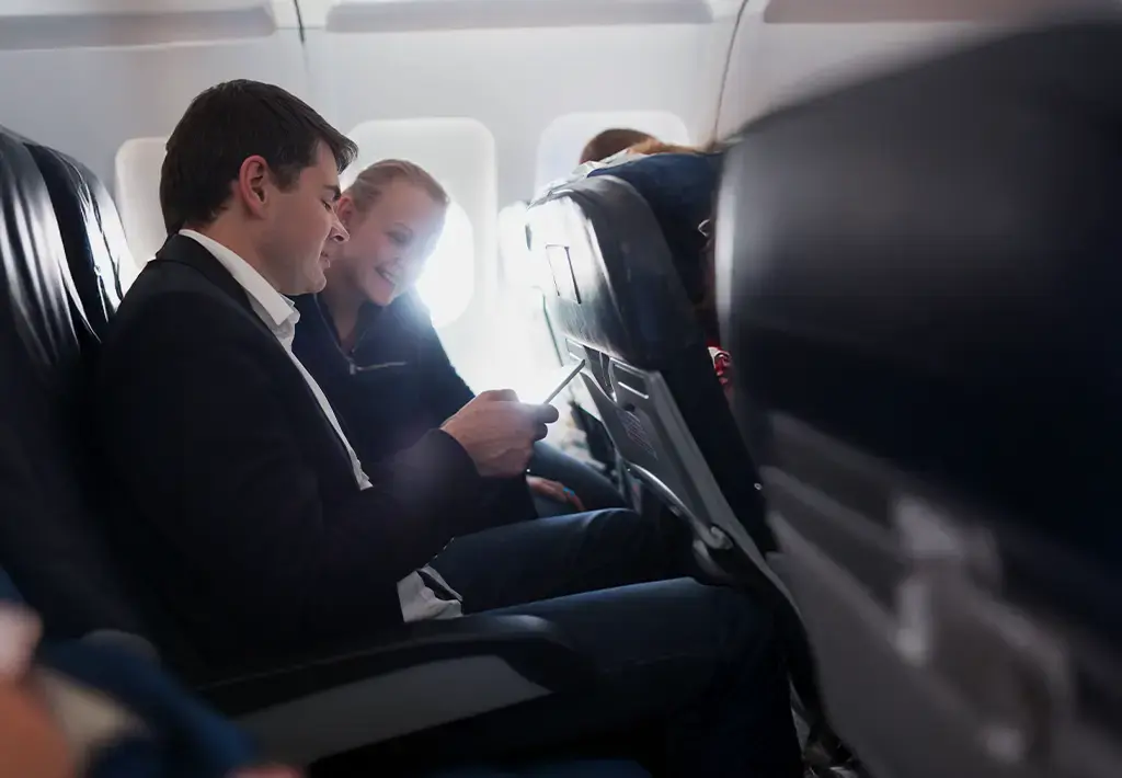 man and woman seated on airplane looking at a mobile phone