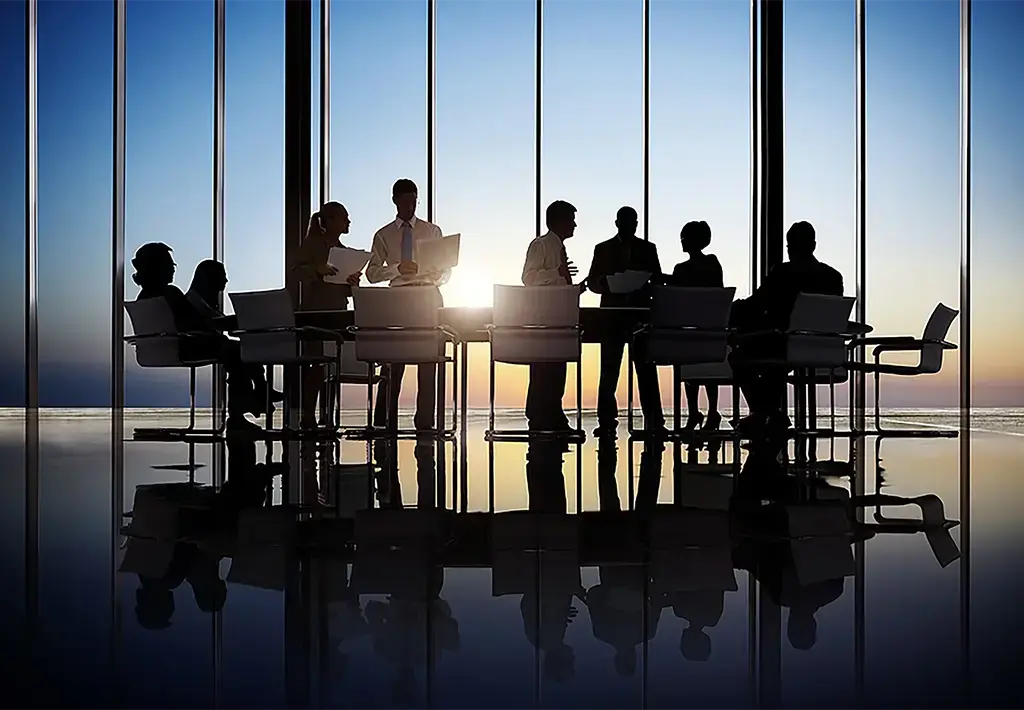 silhouette of people in corporate meeting in front of glass windows with sunset