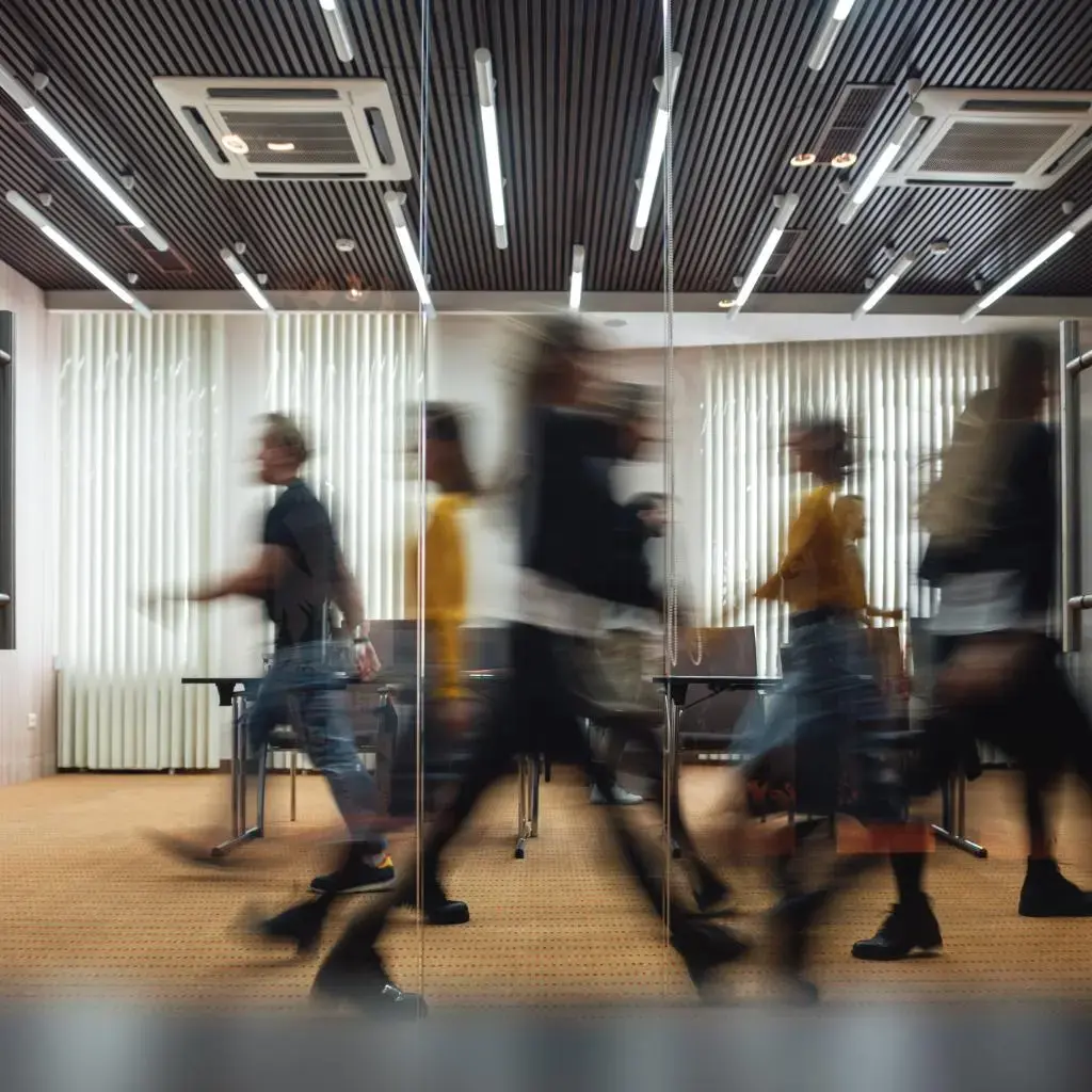 people walking fast down a glass office corridor