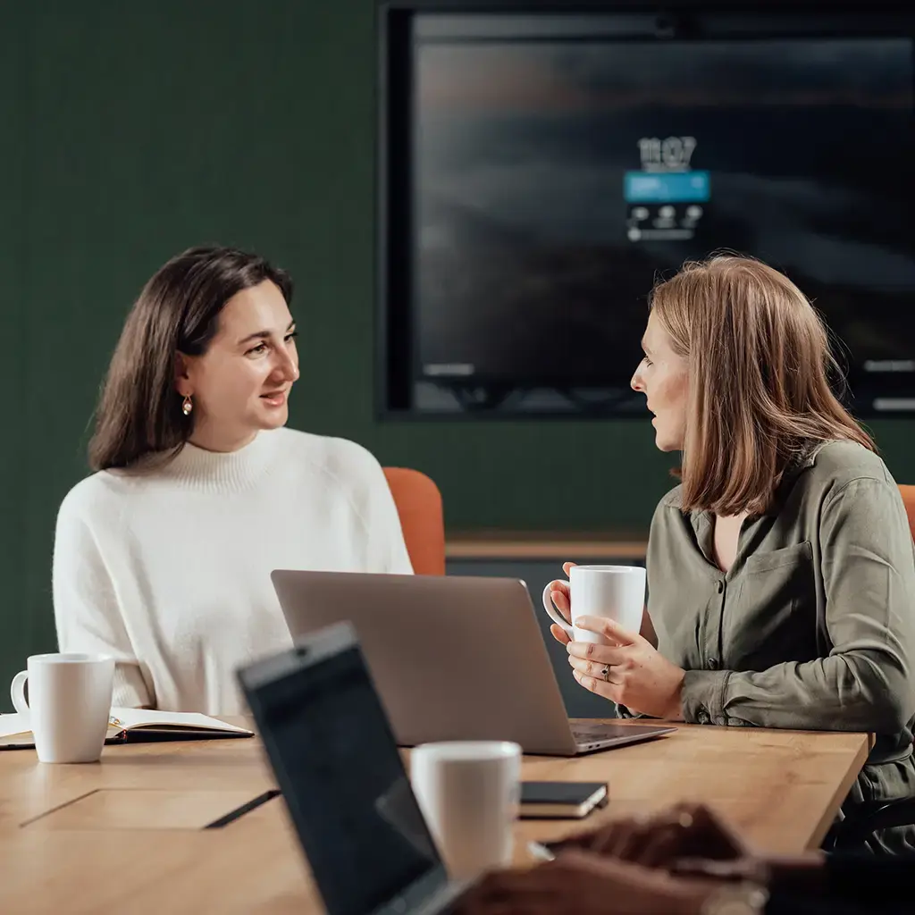 Team members collaborating in a conference room with laptops and a presentation screen in the background.