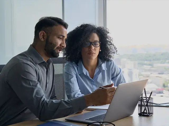 two coworkers in business attire looking at laptop in office