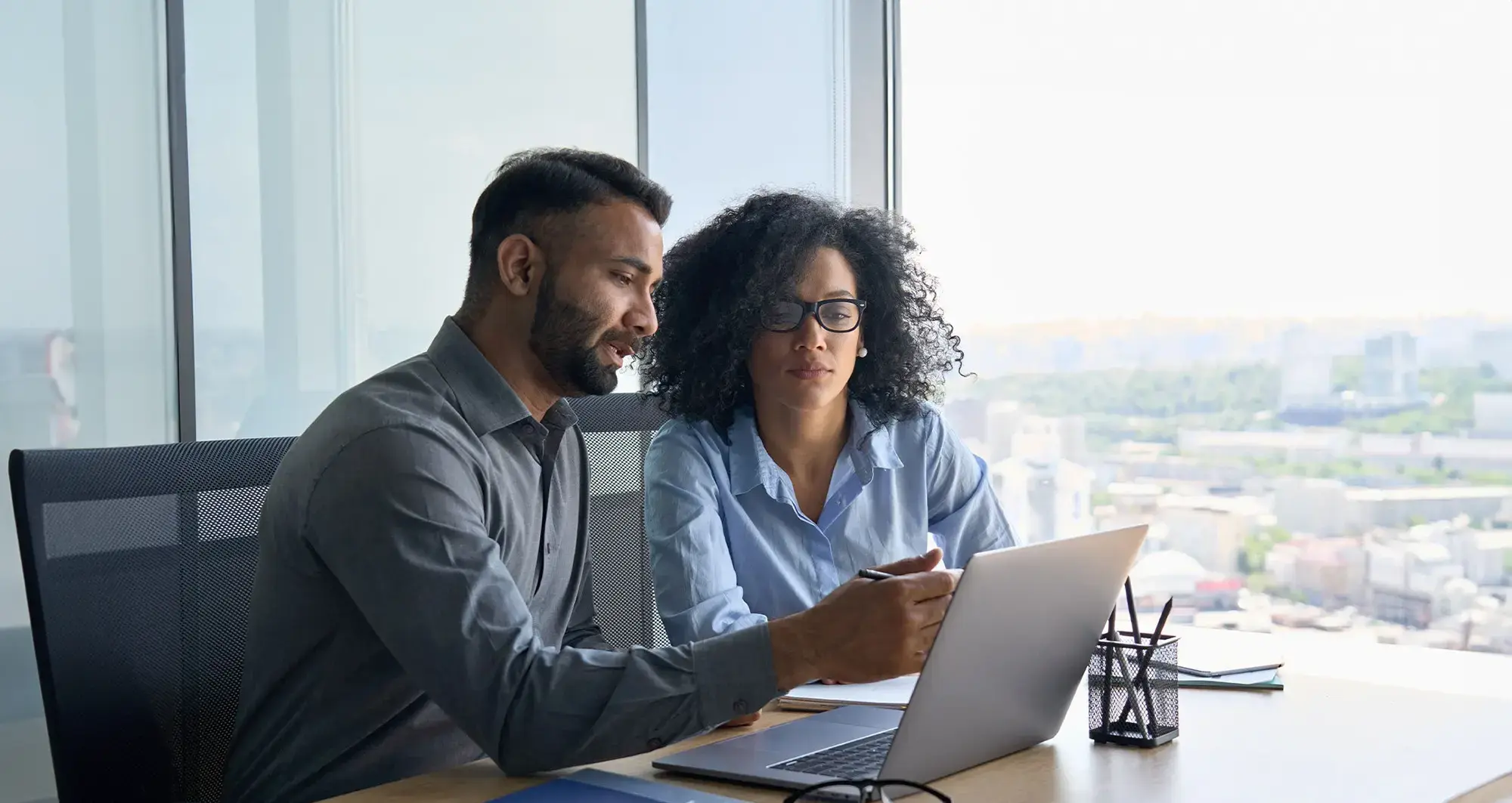 male and female in business attire looking at laptop in office