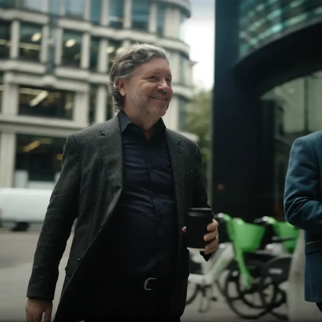 Endava CEO John Cotterell walking through a city with a colleague, both holding coffee cups and engaged in conversation