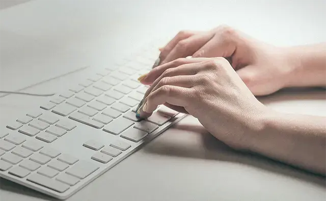 a woman typing on a beige table and keyboard