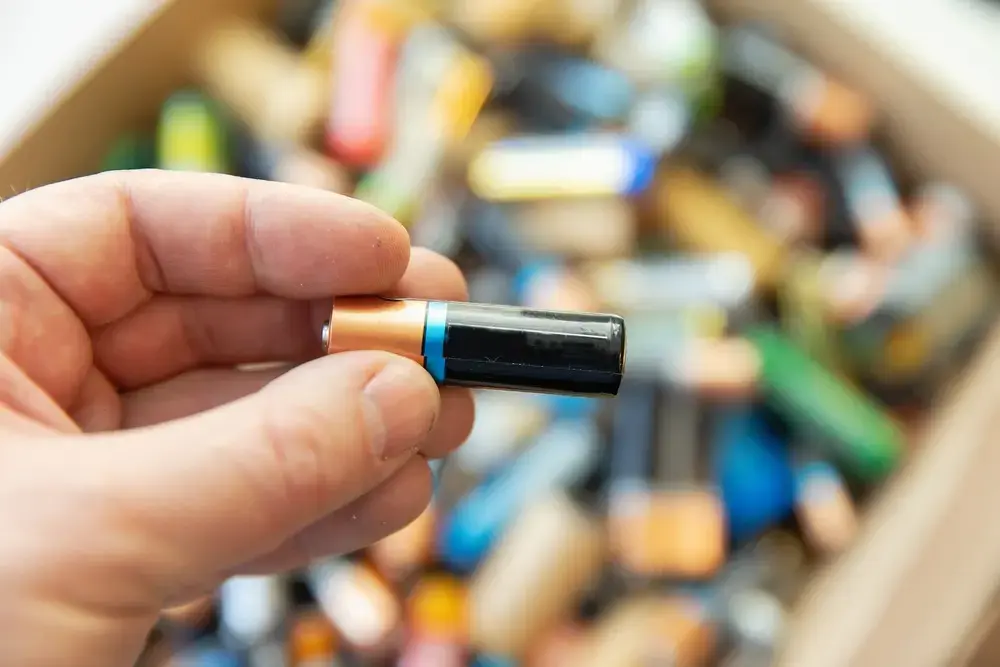 hand holding a single aa battery over a box of old batteries for recycling